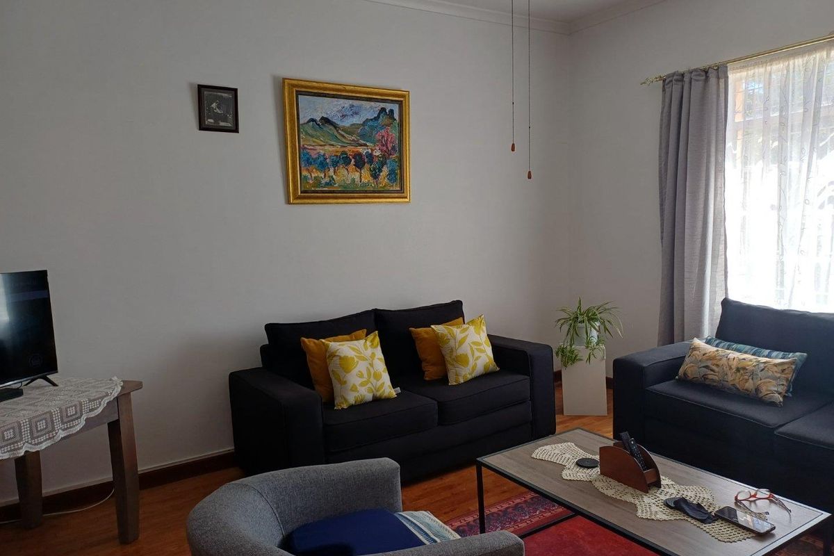 A comfortable living room featuring warm-toned wooden flooring, neutral walls, and natural light provided by a window with curtain treatments.