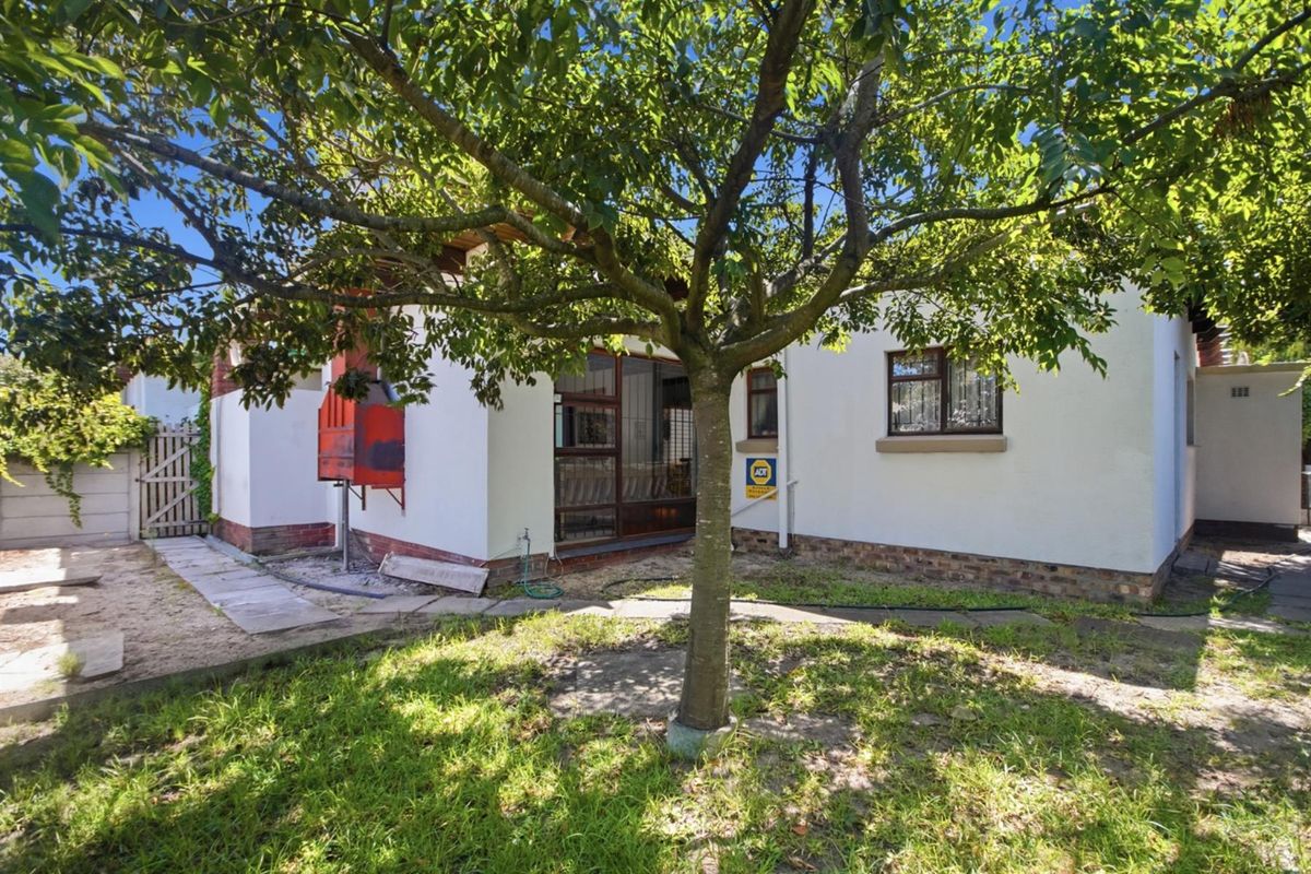 Rear exterior view of the property featuring a garden area, an outdoor fireplace, and access to the home via a security gate.