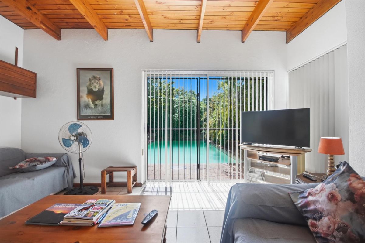 Living room featuring exposed timber beam ceilings, tiled flooring, and a sliding glass door providing direct access to the outdoor pool area.