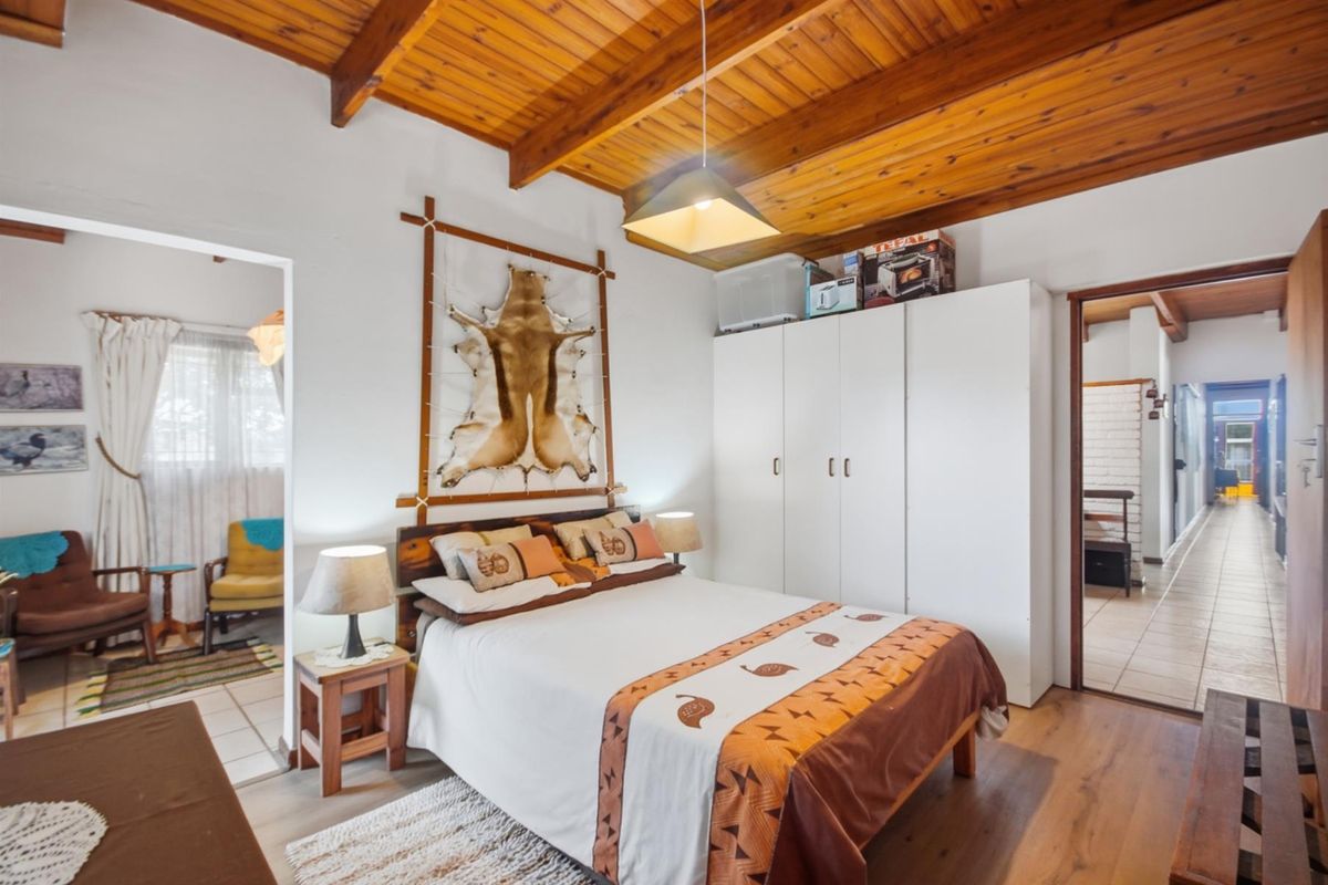A bedroom featuring a vaulted timber ceiling, laminate flooring, and a built-in wardrobe, with direct access to an adjoining room.