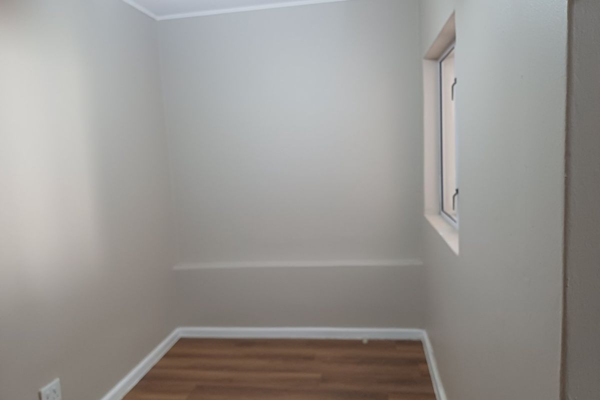 A clean, empty room featuring neutral wall paint, wood-look laminate flooring, and a single window, suitable for use as a bedroom or home office.