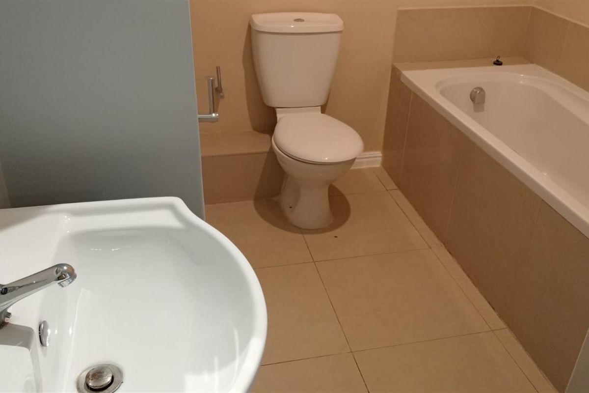 A functional bathroom featuring a standard white toilet, a built-in bathtub with tiled surround, and a pedestal washbasin with chrome faucet.