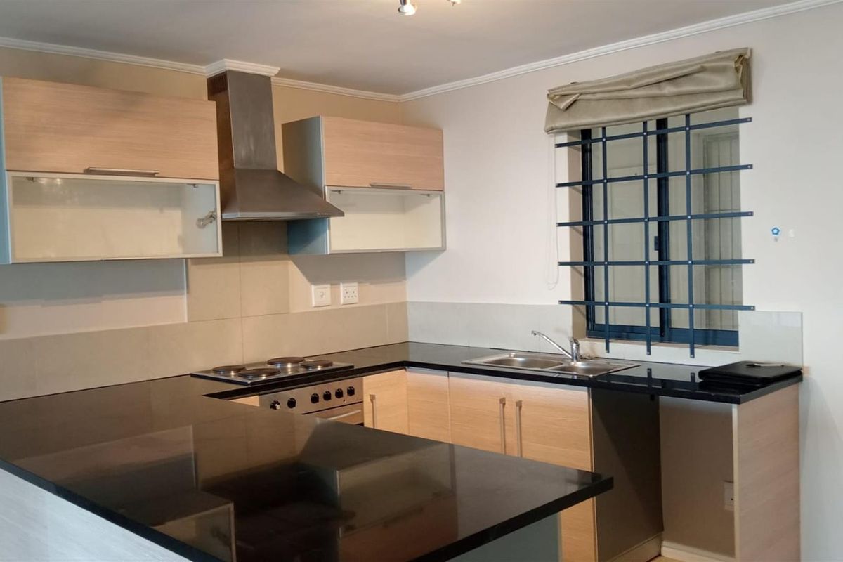 Modern kitchen featuring light wood cabinetry, black granite countertops, a built-in oven with extractor fan, and a double sink with security bars on the window.