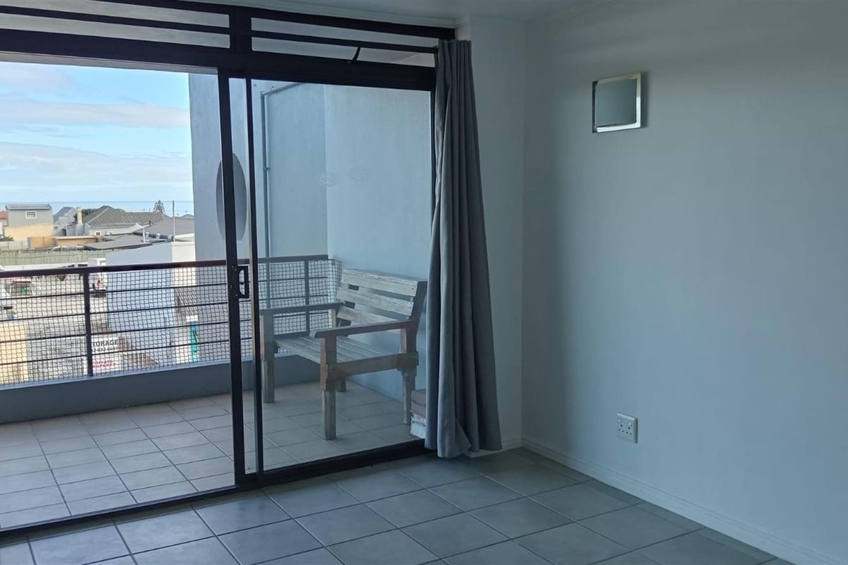 A bright living area featuring large sliding glass doors that open onto a private balcony with tiled flooring and metal railing.