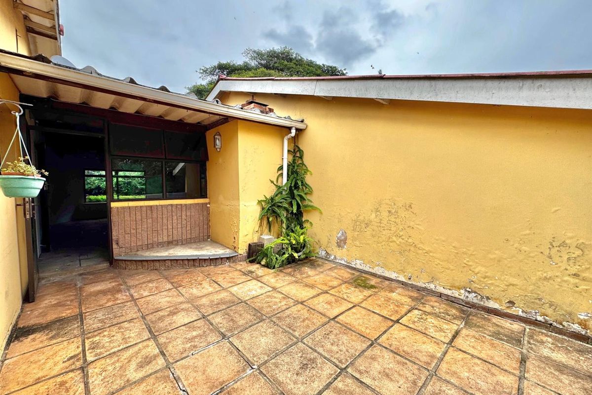 A rear patio area featuring tiled flooring and a yellow exterior wall showing signs of wear and weathering.