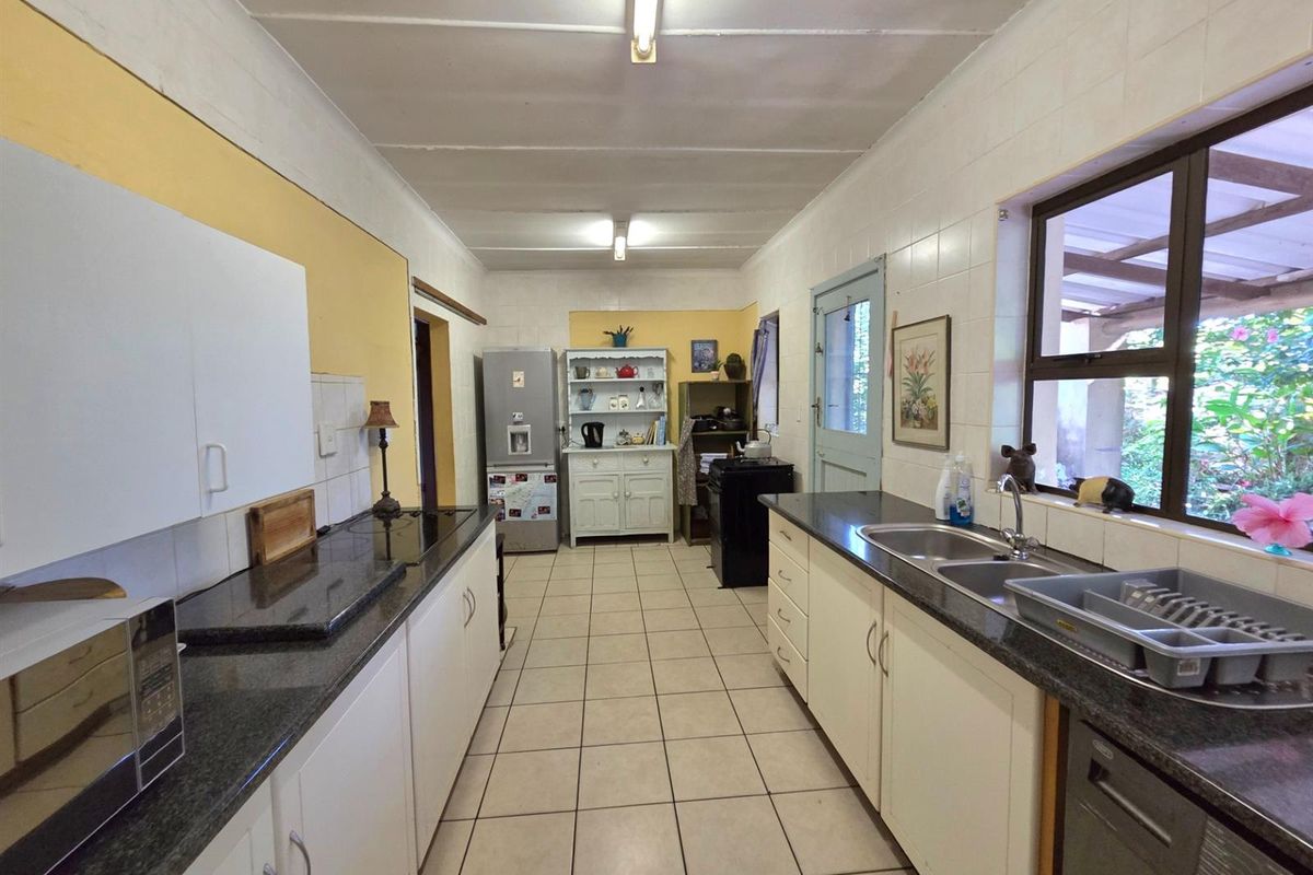 A functional galley-style kitchen featuring granite countertops, white cabinetry, double stainless steel sink, and tiled flooring with direct access to the exterior.
