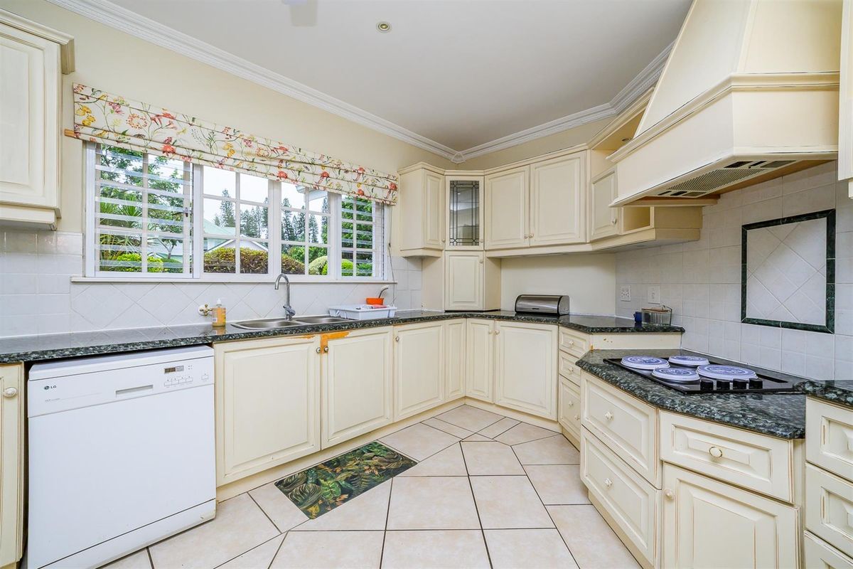 A functional kitchen featuring cream-colored cabinetry, granite countertops, a built-in hob with extractor fan, and tiled flooring.