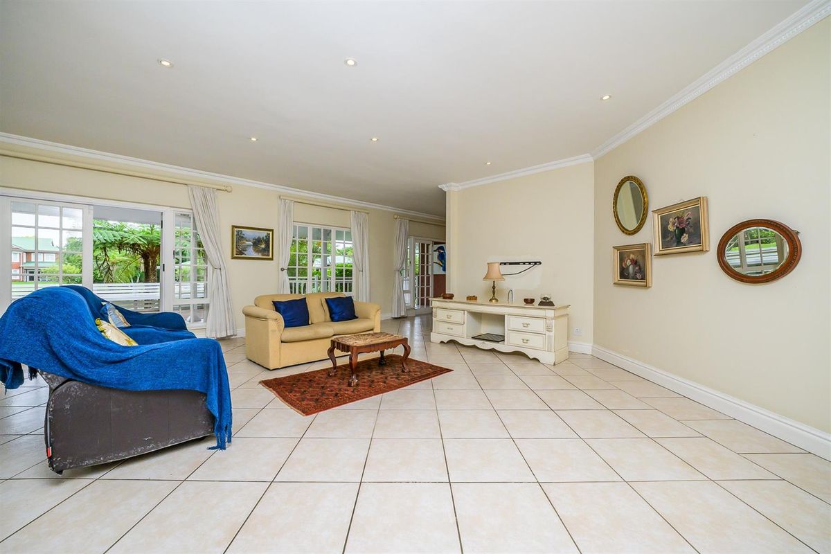 Spacious living room featuring neutral ceramic floor tiles, recessed downlighting, crown molding, and multiple glass-paneled doors providing access to the outdoor patio area.