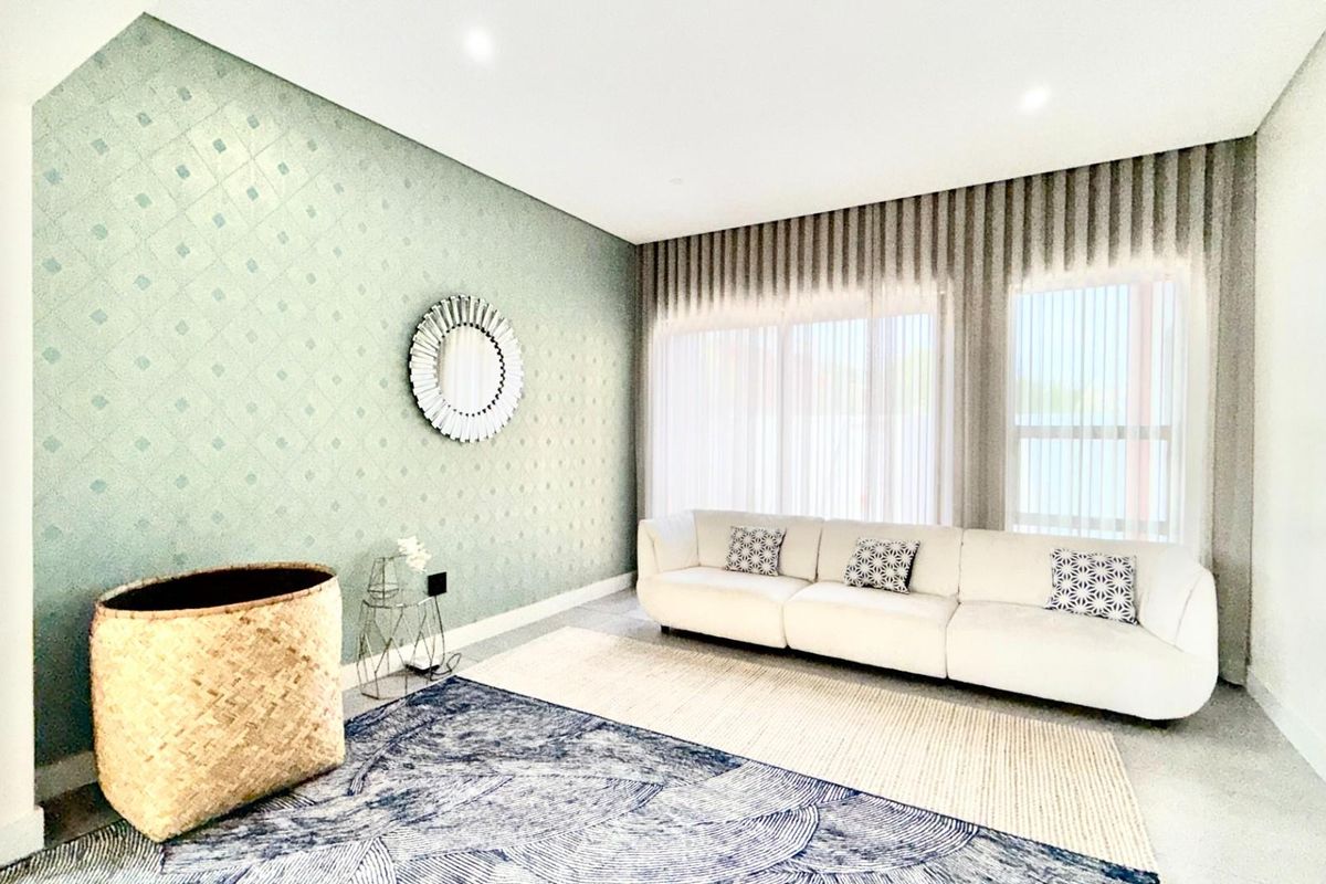A bright and modern living room featuring a textured accent wall, recessed ceiling lighting, and large windows with floor-to-ceiling curtains.