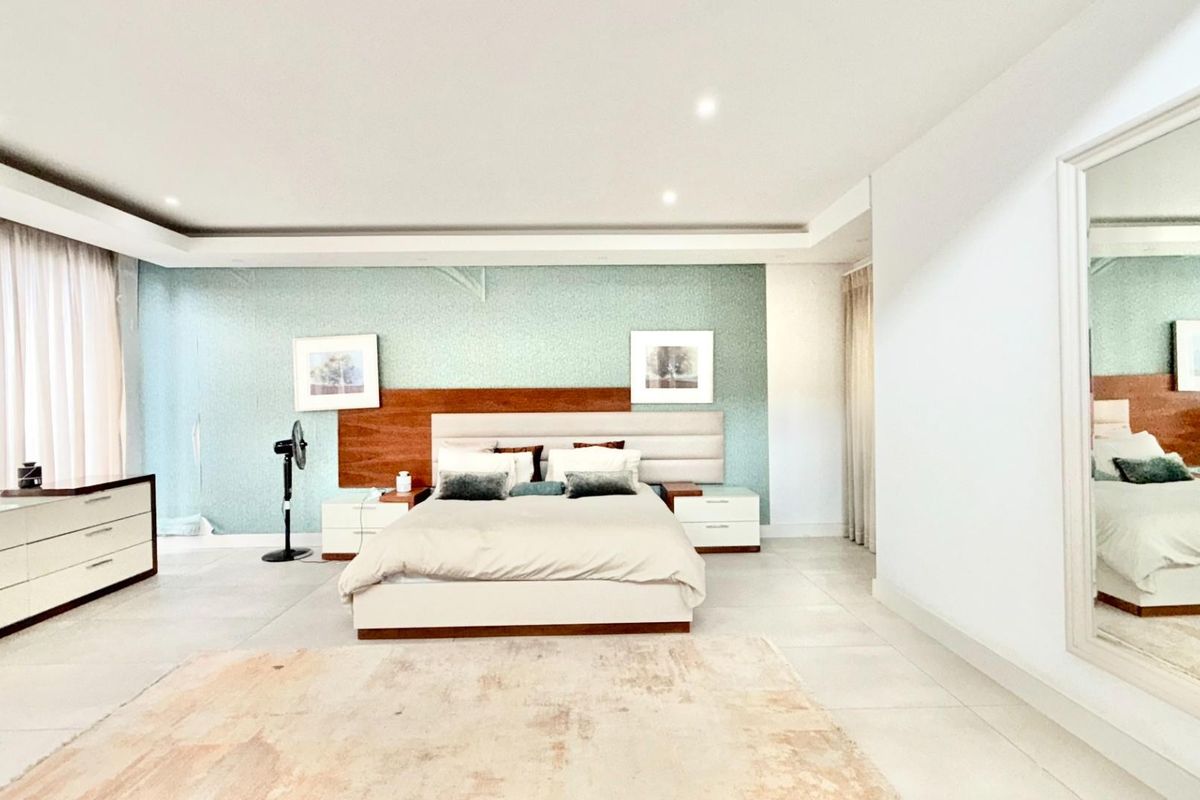 Spacious primary bedroom featuring a built-in headboard, recessed ceiling lighting, and large format floor tiles.