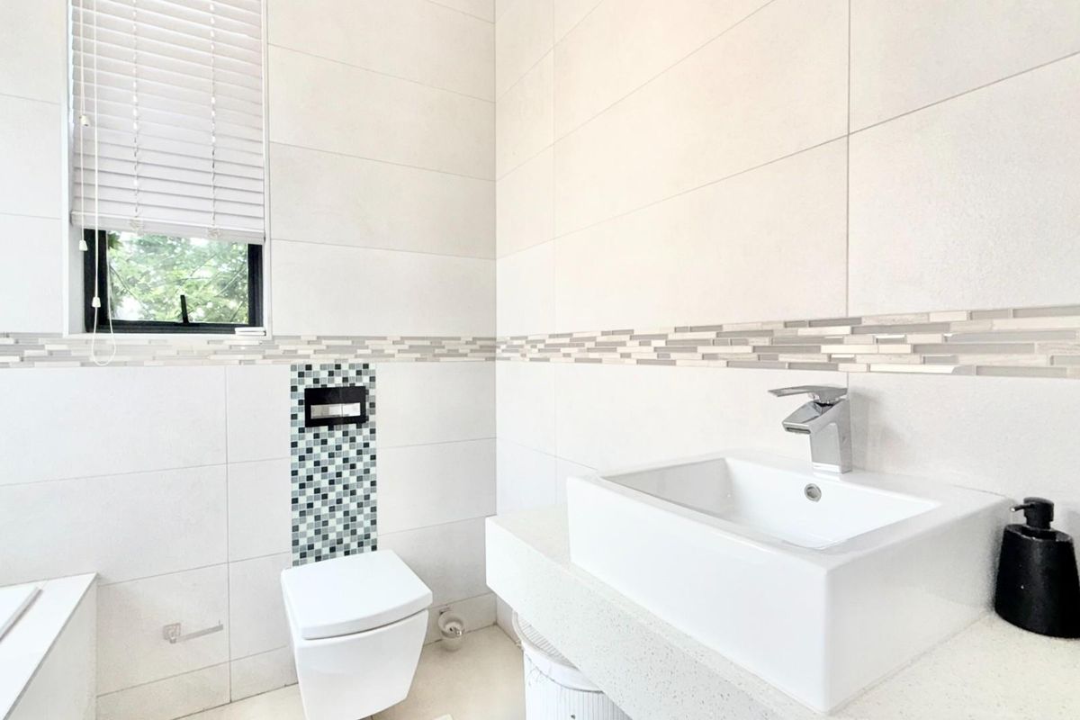 Modern bathroom featuring a wall-mounted toilet, vessel sink with chrome faucet, and decorative mosaic tile accents.