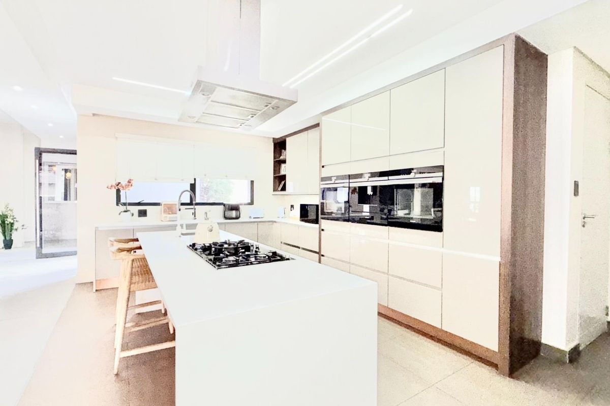 Modern kitchen featuring a large central island with integrated gas hob, sleek cabinetry, built-in ovens, and a stainless steel extractor fan.
