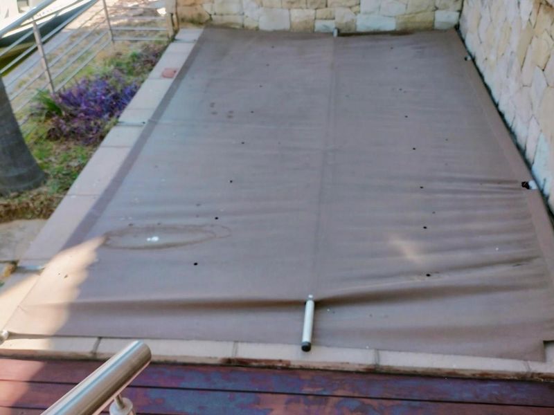A view of a swimming pool covered with a protective safety cover, situated adjacent to a stone-clad wall and timber decking.