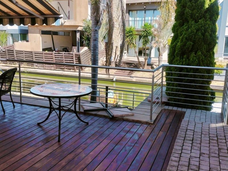 A covered outdoor patio featuring timber decking, stainless steel balustrades, and a retractable awning, overlooking a canal-side setting.