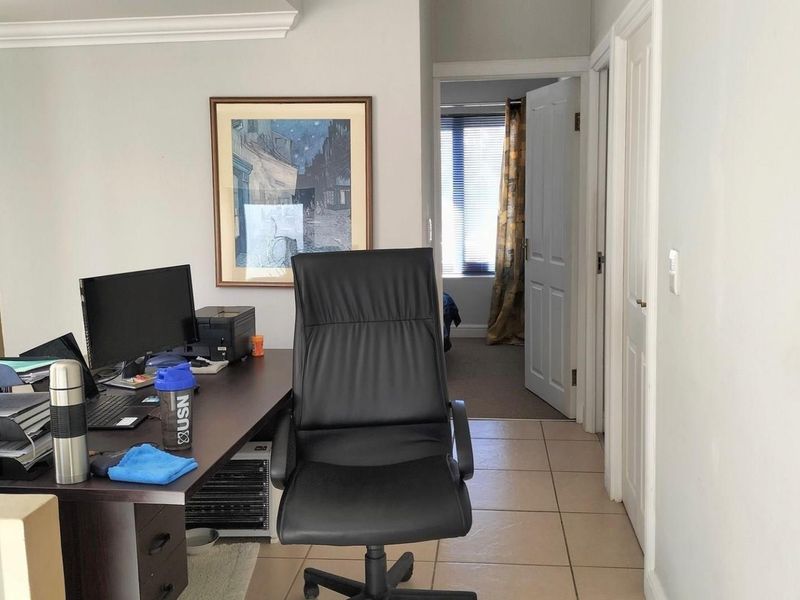 A functional home office space featuring tiled flooring and access to an adjacent room through a standard interior door.