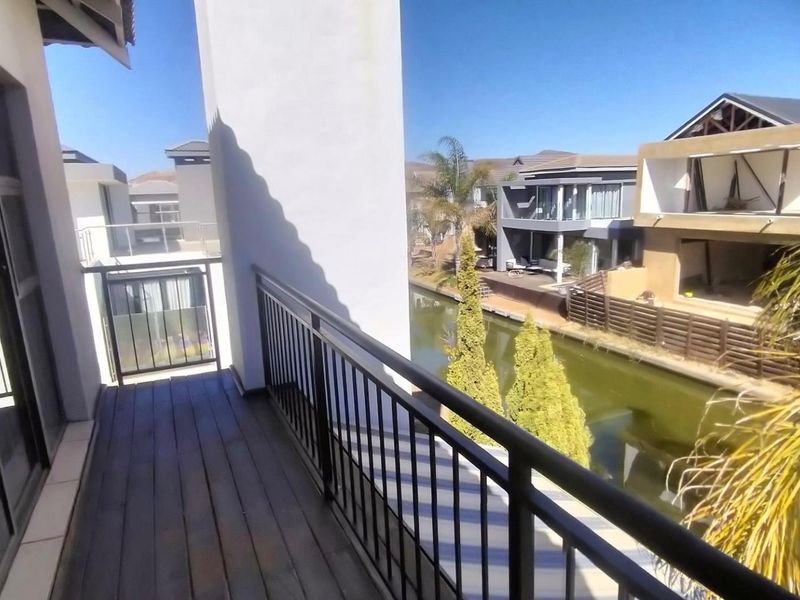 A balcony with timber decking and metal railings overlooking a canal and neighbouring residential properties.