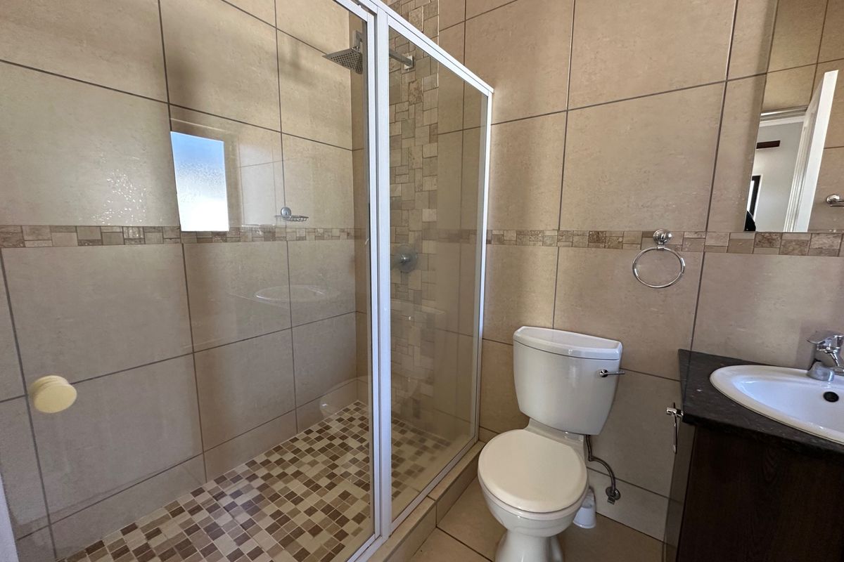 A clean, functional bathroom featuring a glass-enclosed shower, neutral wall tiling with mosaic accents, a vanity basin, and a standard toilet.