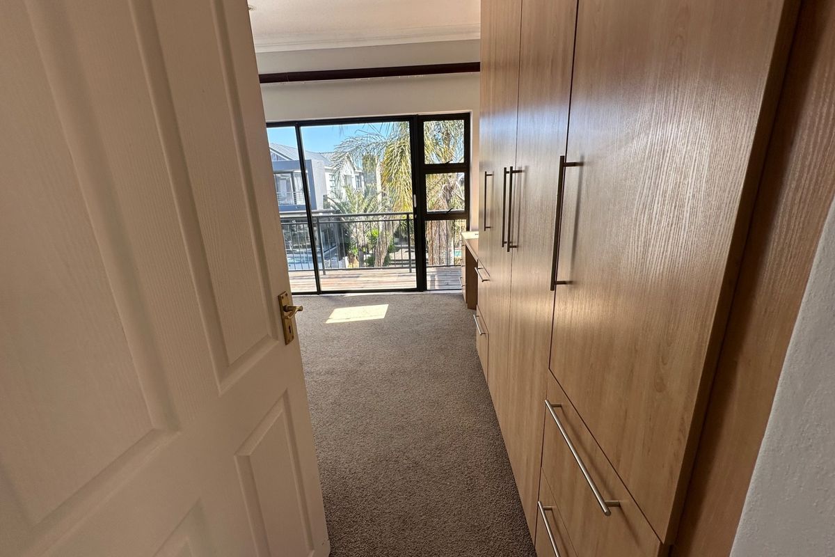 A bright bedroom featuring extensive built-in wooden cabinetry, neutral carpeting, and a large sliding glass door providing access to an outdoor balcony area.