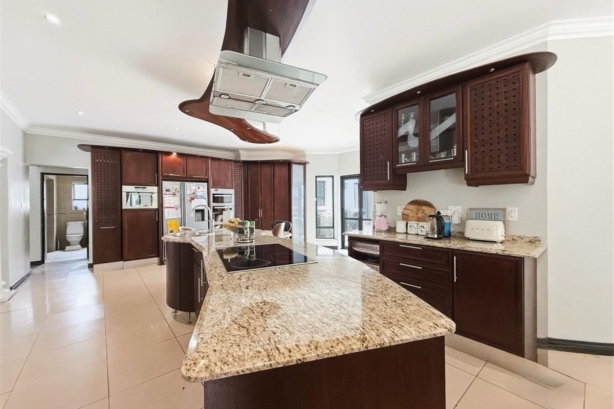 Spacious kitchen featuring dark wood cabinetry, granite countertops, a central island with a built-in cooktop, and integrated appliances.