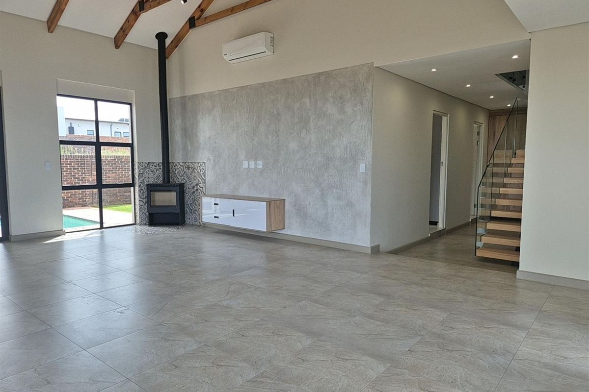 Spacious living area featuring high vaulted ceilings with exposed timber trusses, a modern fireplace, tiled floors, and a sleek staircase with glass balustrades.