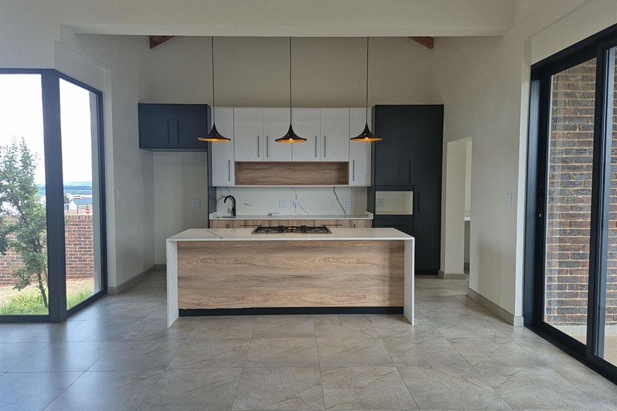 Modern open-plan kitchen featuring a central island with a gas hob, sleek two-tone cabinetry, stone countertops, and large sliding doors leading to the exterior.