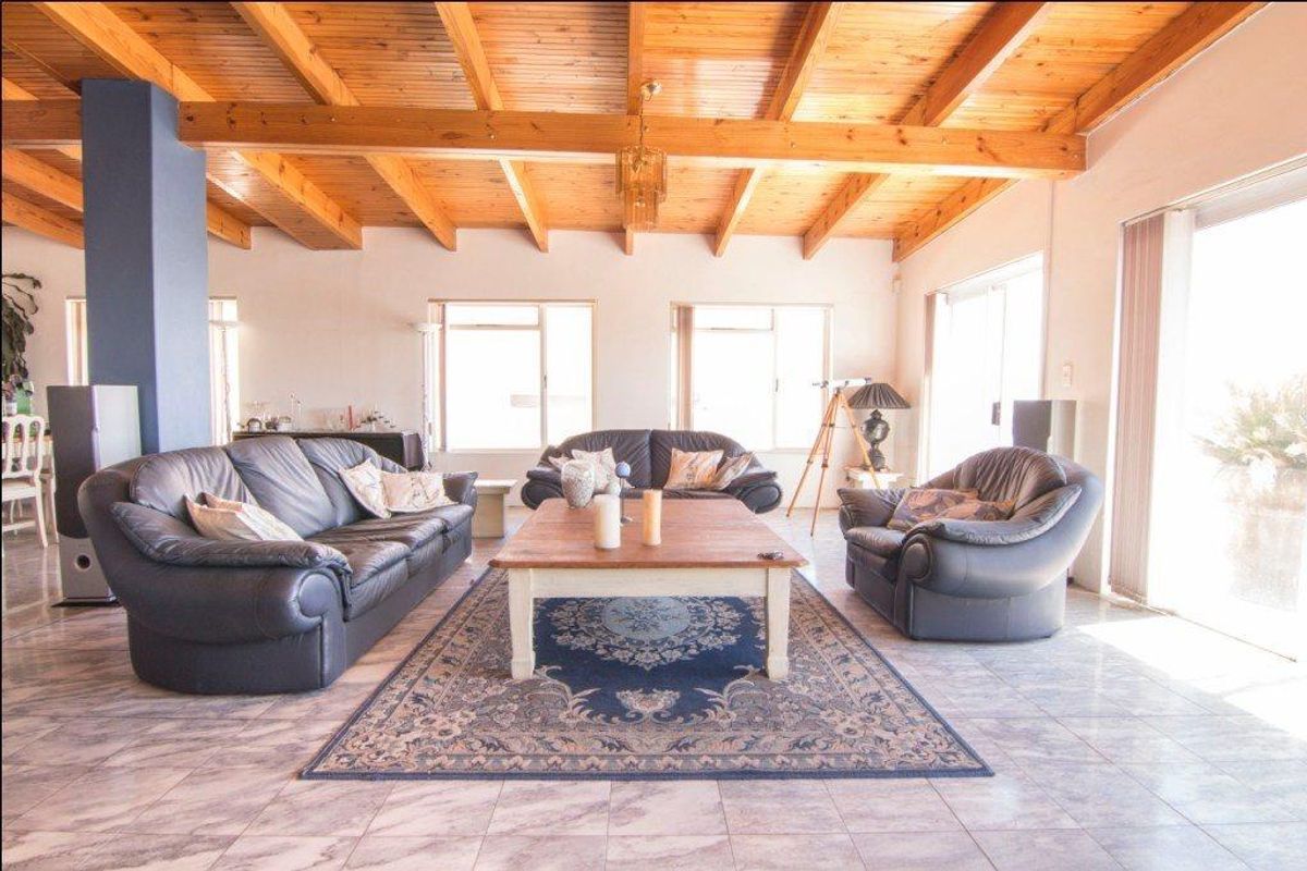 Spacious living room featuring exposed timber beam ceilings, large windows providing natural light, and tiled flooring throughout.