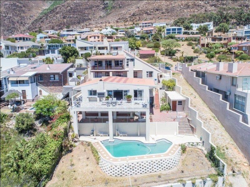 Aerial view of a multi-level residential property featuring a swimming pool, elevated patio deck, and terraced garden area in a hillside neighborhood.