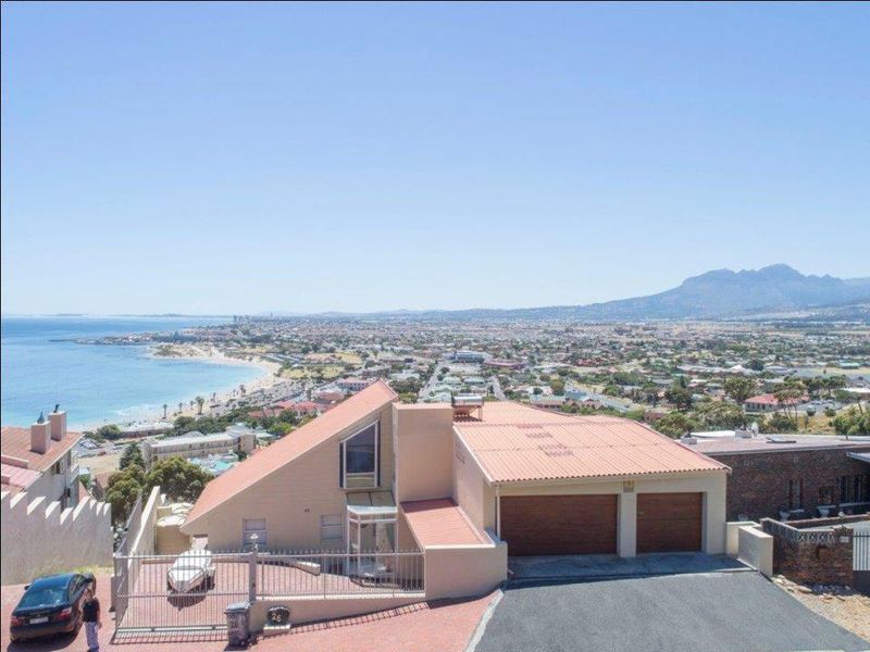 Elevated aerial view of a coastal property featuring a double garage, paved driveway, and expansive ocean and mountain vistas.
