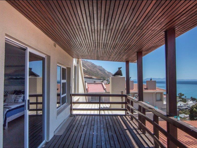 A covered balcony featuring timber decking and a slatted wood ceiling, offering elevated views of the surrounding neighborhood and the ocean.
