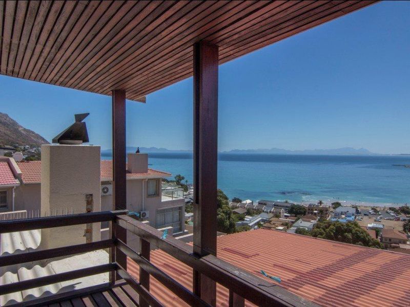 A covered balcony featuring timber ceiling and railing, offering expansive panoramic views of the coastline and ocean.