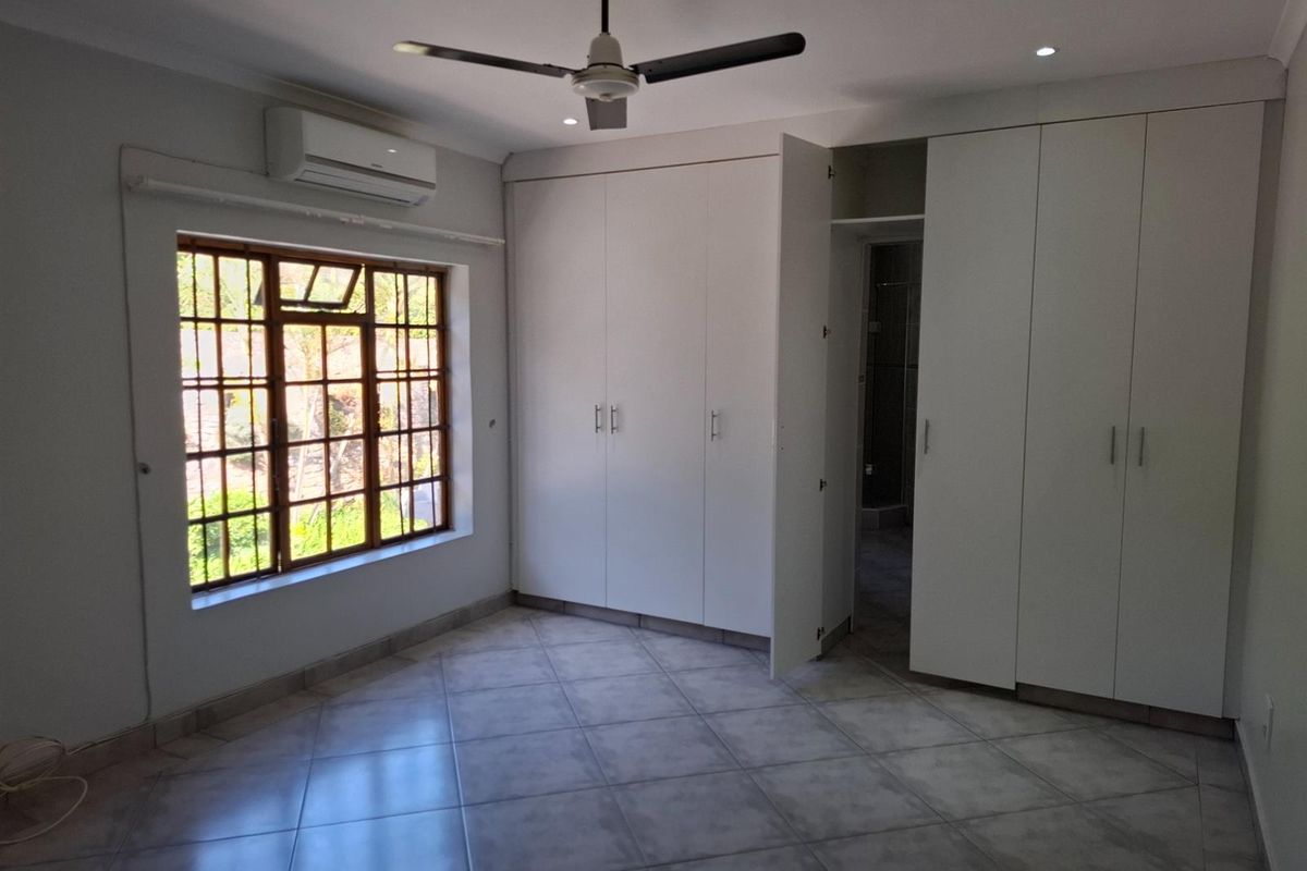 A bright bedroom featuring built-in wardrobes, tiled flooring, a ceiling fan, and a wall-mounted air conditioning unit.