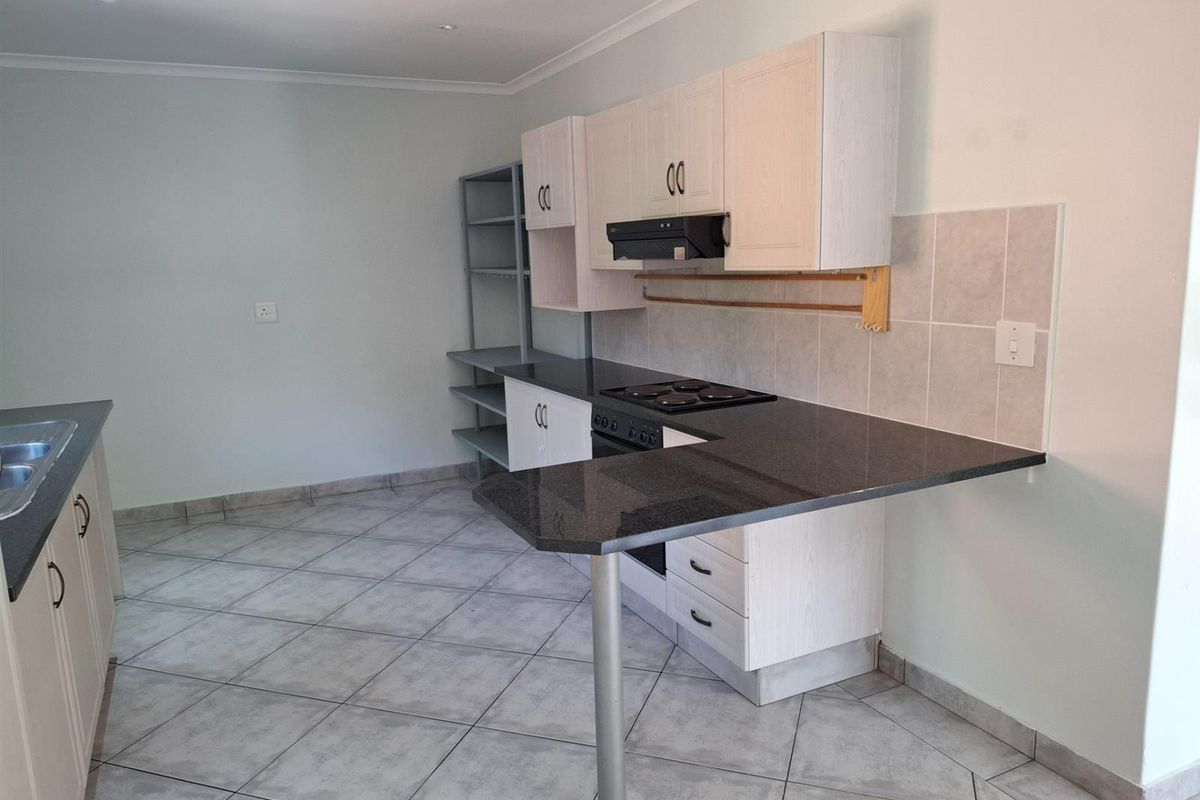 Functional kitchen featuring dark granite countertops, built-in hob and oven, light-toned cabinetry, and tiled flooring with a breakfast bar extension.
