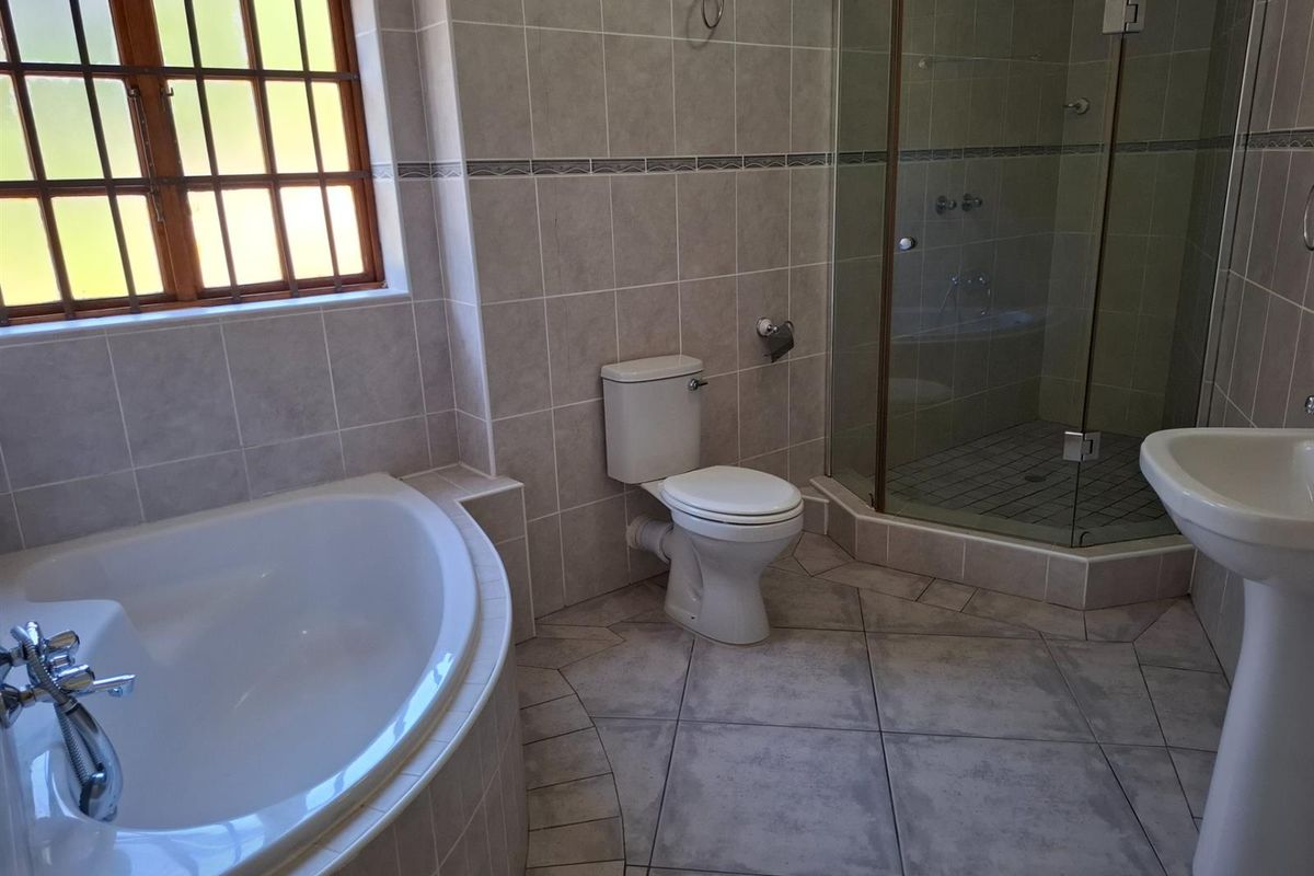 A functional bathroom featuring a corner bathtub, a separate glass-enclosed shower, a pedestal basin, and a toilet with neutral wall and floor tiling.