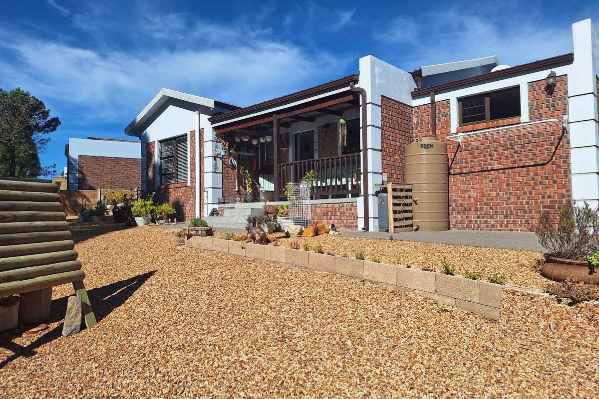 Exterior view of the rear facade featuring a covered patio, brick masonry walls, and a water storage tank set within a gravel garden area.