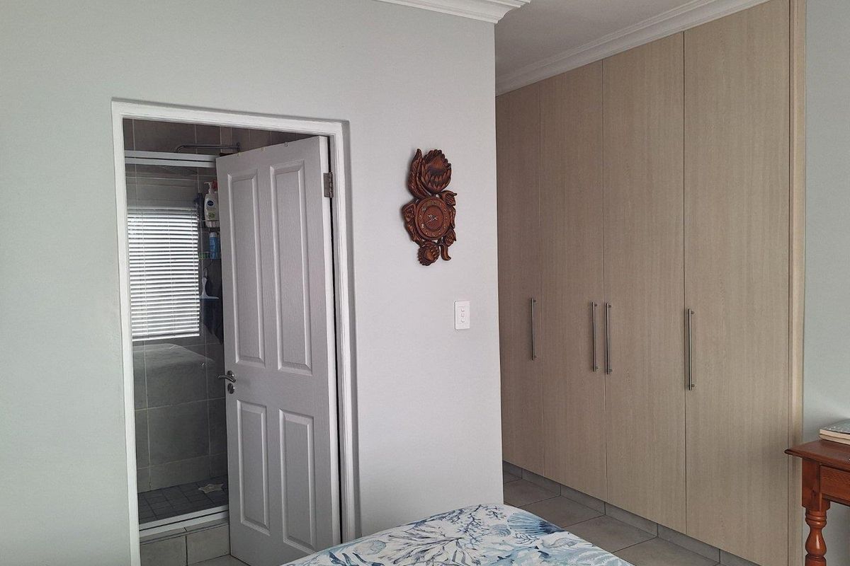 Bedroom featuring built-in light wood cabinetry and an en-suite bathroom with a shower, finished with neutral wall tones and tiled flooring.