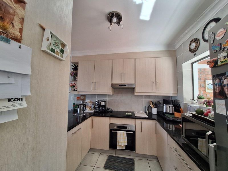 A functional U-shaped kitchen featuring light wood-grain cabinetry, dark granite countertops, tiled backsplash, and built-in stainless steel oven and extractor fan.