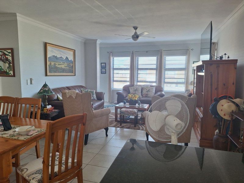 An open-plan living and dining area featuring tiled flooring, large windows with blinds, and a ceiling fan, creating a comfortable and functional living space.