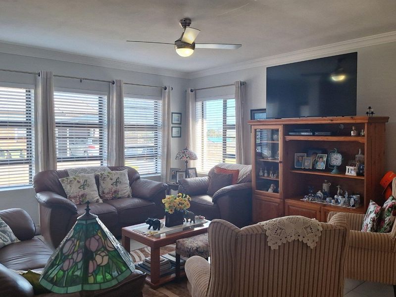 A comfortable living room featuring large windows with fitted blinds, a ceiling fan, and crown molding, providing a bright and inviting space.