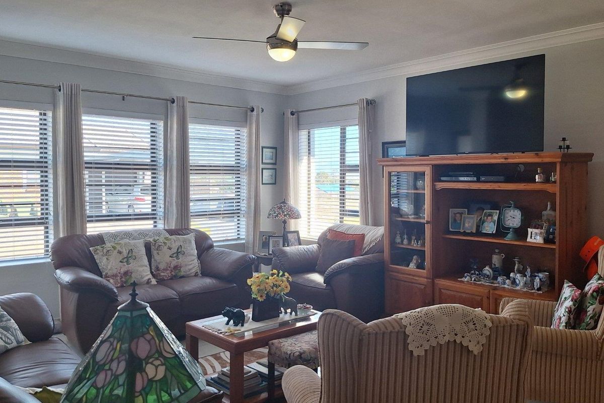 A comfortable living room featuring large windows with fitted blinds, a ceiling fan, and crown molding, providing a bright and inviting space.