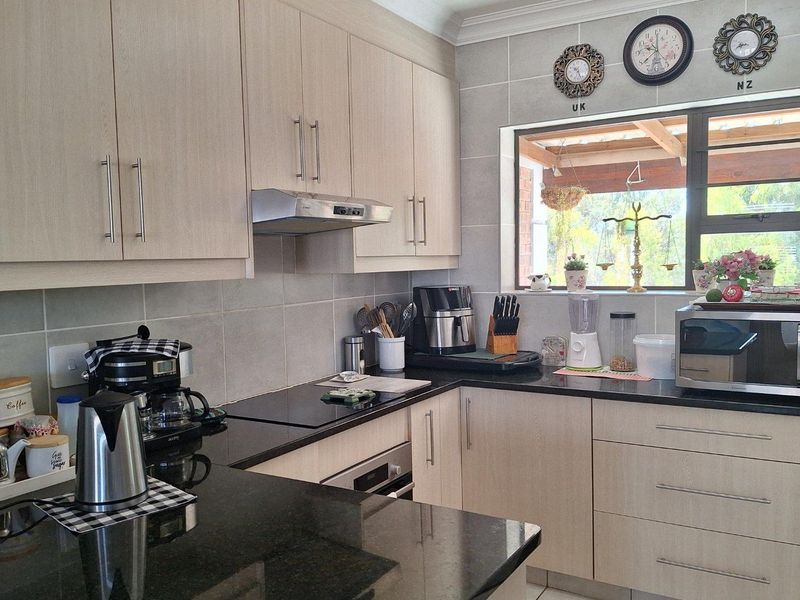 A functional kitchen featuring light wood-grain cabinetry, dark granite countertops, tiled backsplash, and built-in stainless steel oven and extractor fan.
