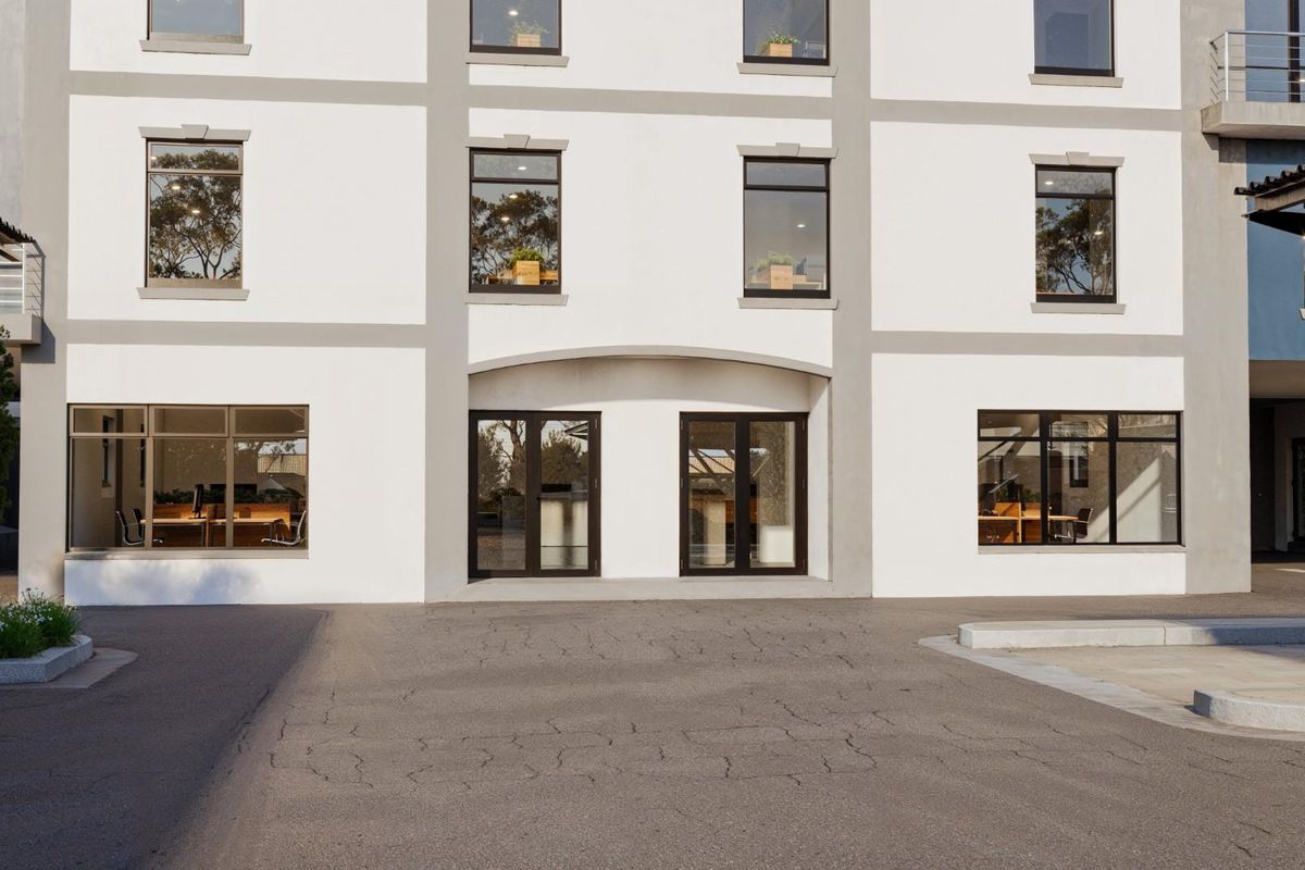 Front facade of a commercial building featuring a clean white exterior, large aluminium-framed windows, and a paved driveway with a covered entrance.