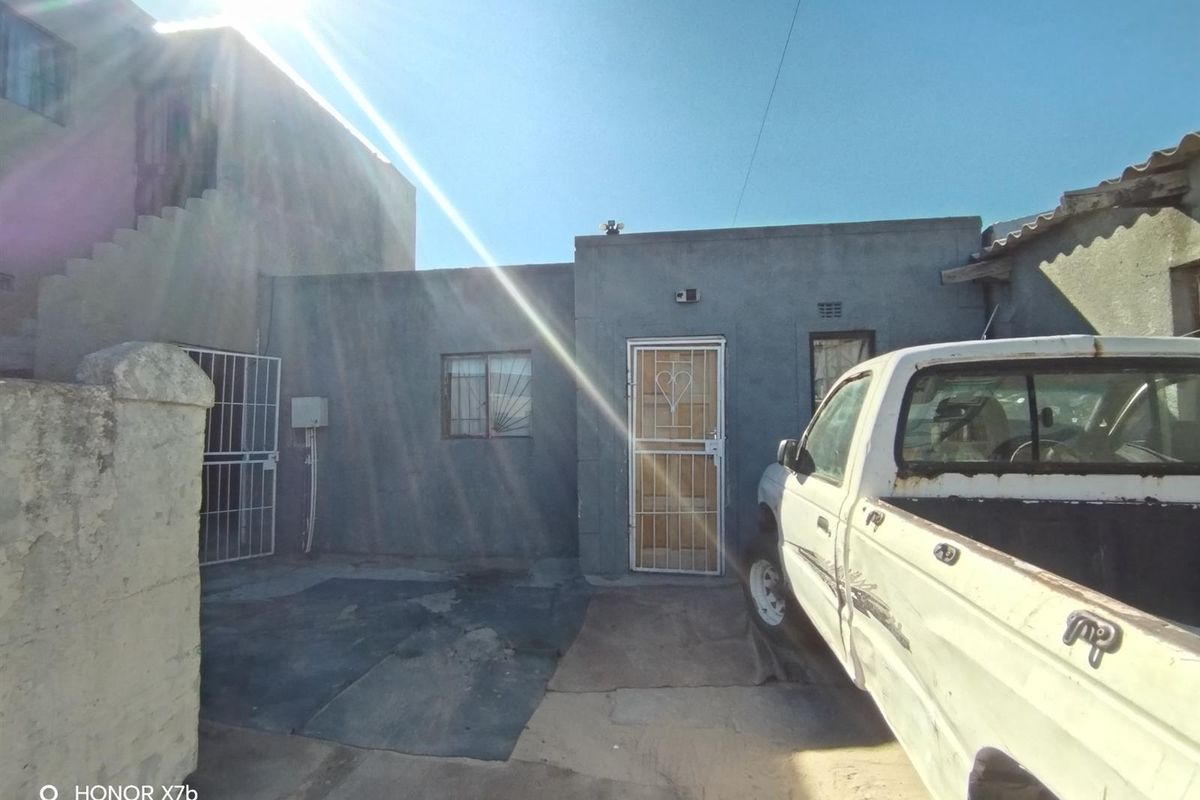 Rear exterior view of the property featuring a concrete paved area, security gates, and basic wall finishes.