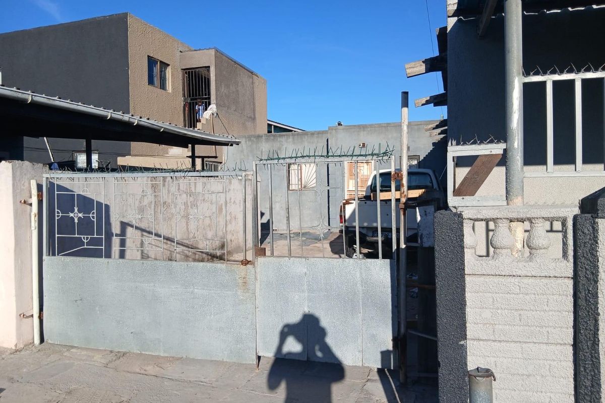 Front exterior view of the property featuring a metal security gate, perimeter wall with razor wire, and a carport structure.