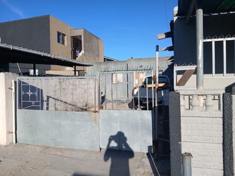 Front exterior view of the property featuring a metal security gate, perimeter wall with razor wire, and a carport structure.