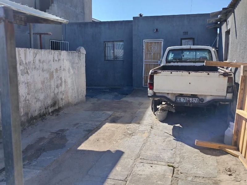 Rear exterior area featuring concrete paving and a boundary wall, showing signs of significant wear and weathering.