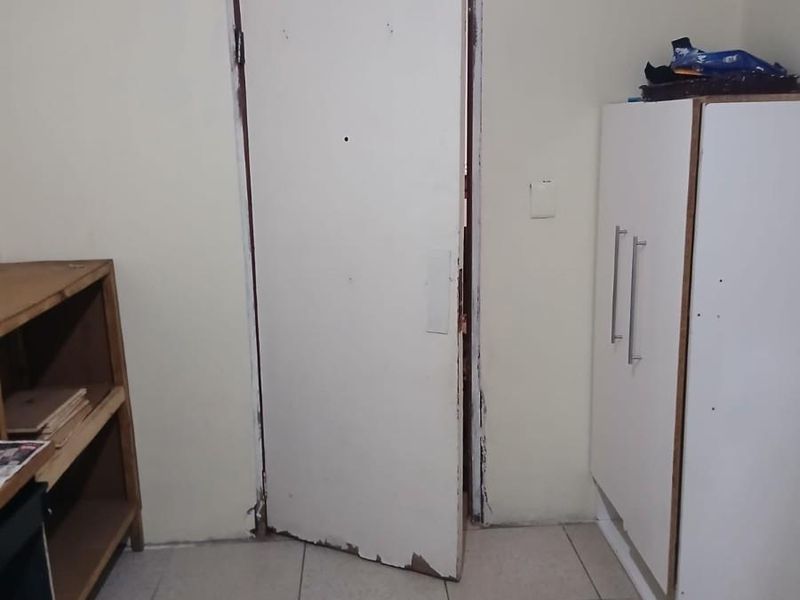 A small bedroom featuring tiled flooring and a white door with visible wear and tear on the frame and surface.