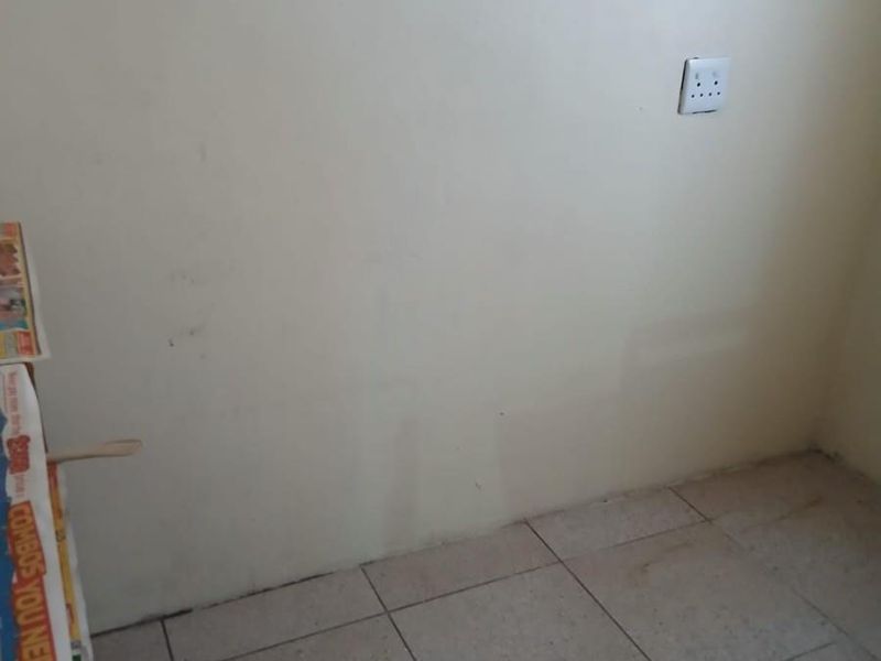 An empty corner space featuring plain walls, ceramic floor tiles, and a single electrical outlet.