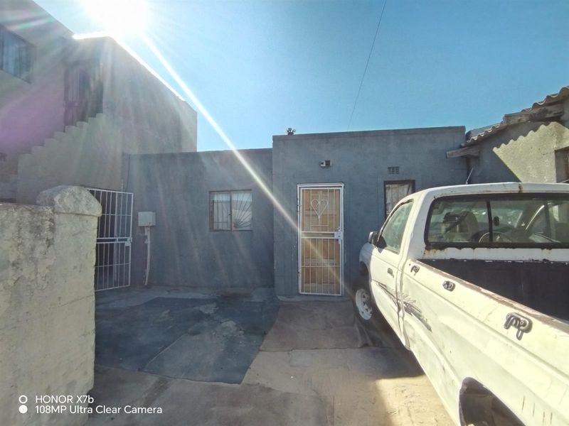 Rear exterior view of the property featuring a concrete paved area, security gates, and basic wall finishes.