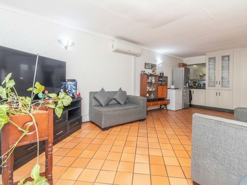 Open-plan living area featuring terracotta floor tiles, wall-mounted air conditioning, and integrated kitchen cabinetry, offering a functional and connected living space.