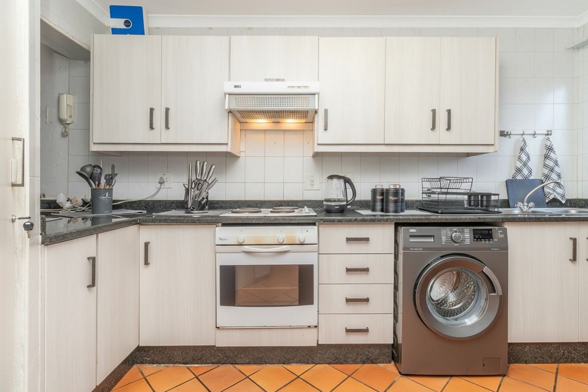 Functional kitchen featuring light-toned laminate cabinetry, granite countertops, built-in oven with extractor fan, and durable terracotta floor tiles.